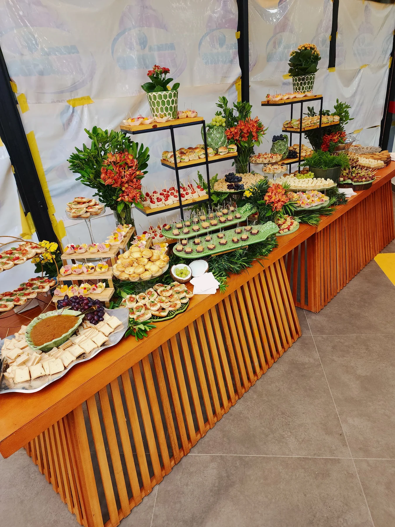 Mesa de aperitivos com flores, frutas e bandejas em diferentes alturas na festa de debutante.