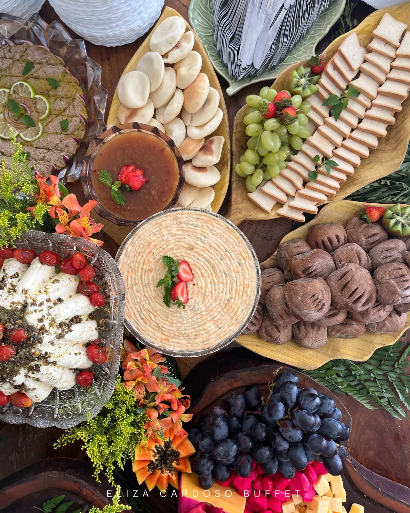 Composição de queijos, frutas e aperitivos servida na mesa de frios da recepção.