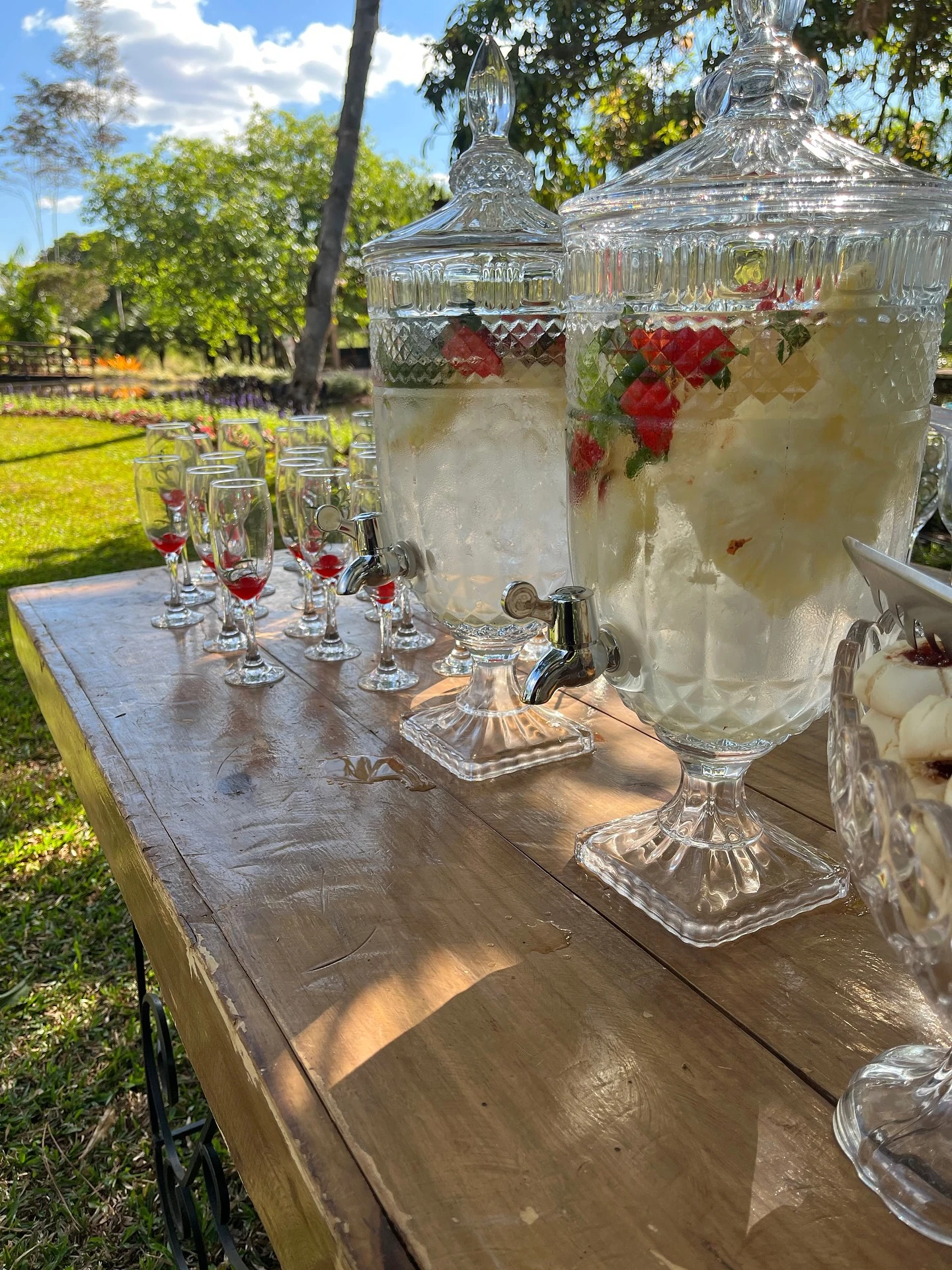 Jarras de vidro com frutas e bebidas sobre mesa ao ar livre em evento corporativo.