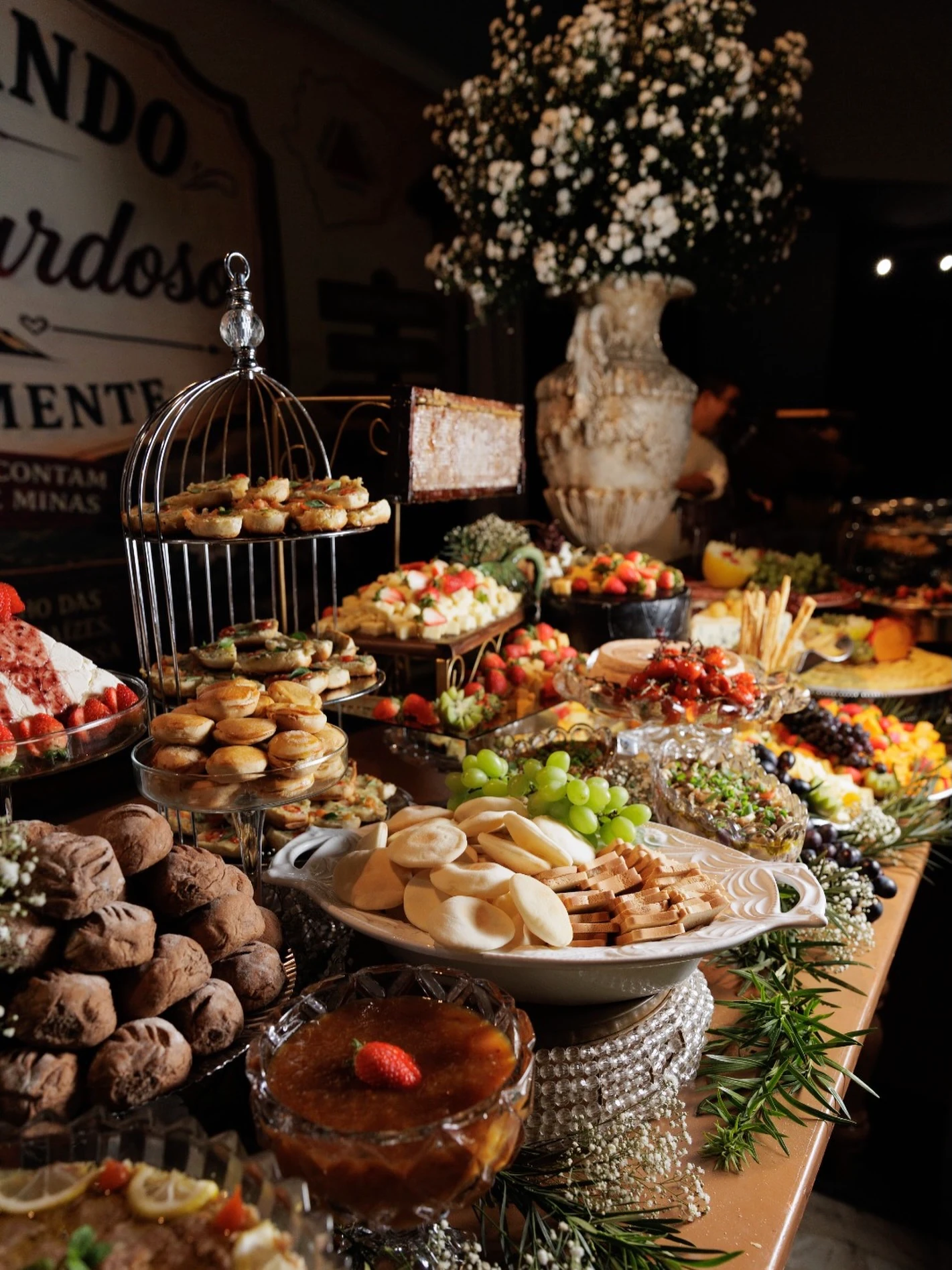 Mesa farta de recepção de casamento com doces, frutas e travessas em vários níveis.