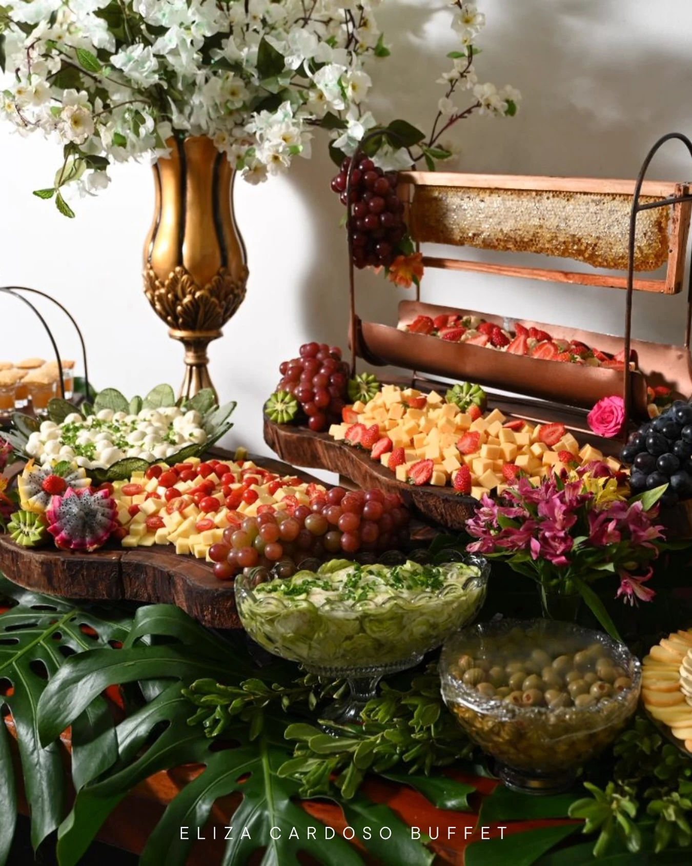Mesa alta com flores brancas e tábua de frios no coquetel de recepção.