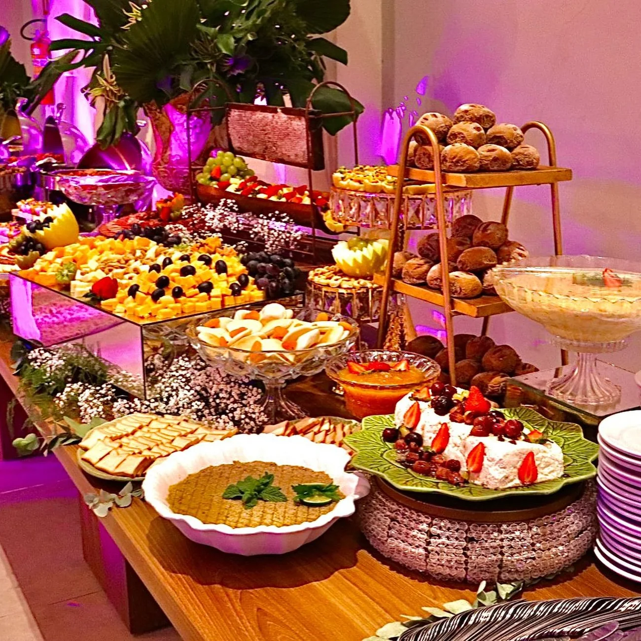 Mesa de festa montada com travessas, flores e aperitivos variados.