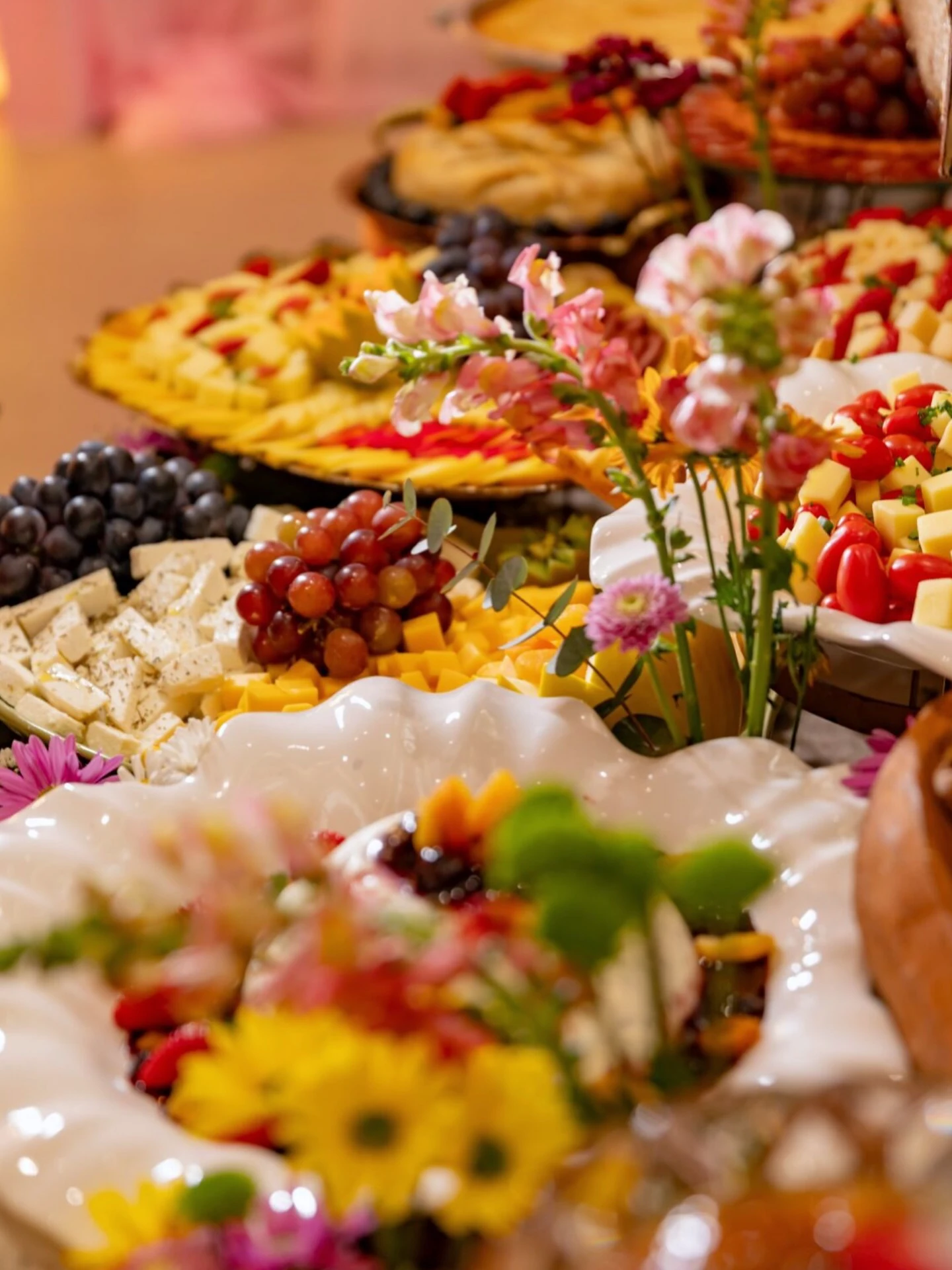 Mesa de festa de quinze anos com tortas, frutas e flores coloridas.