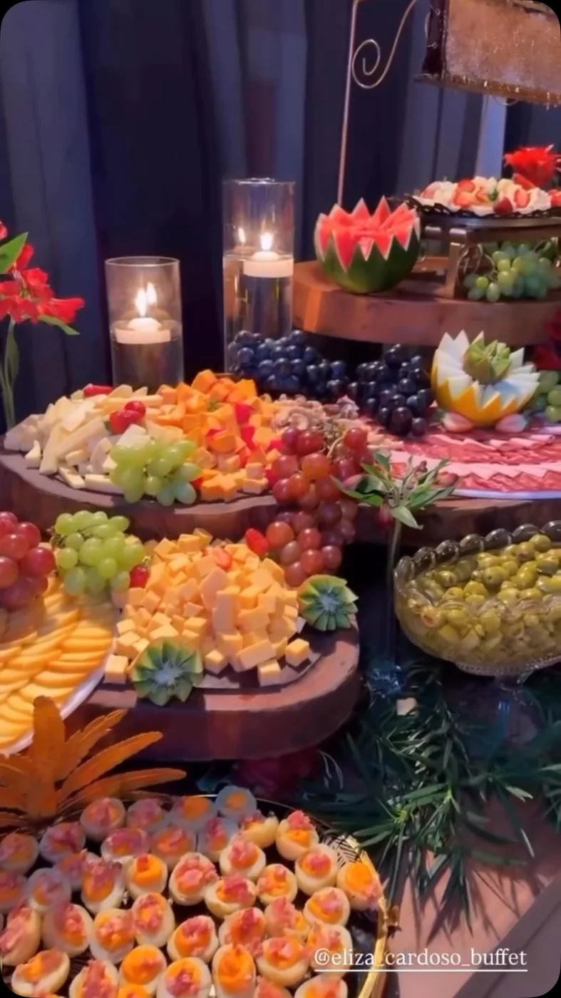 Mesa de frios e frutas iluminada por velas durante a recepção.